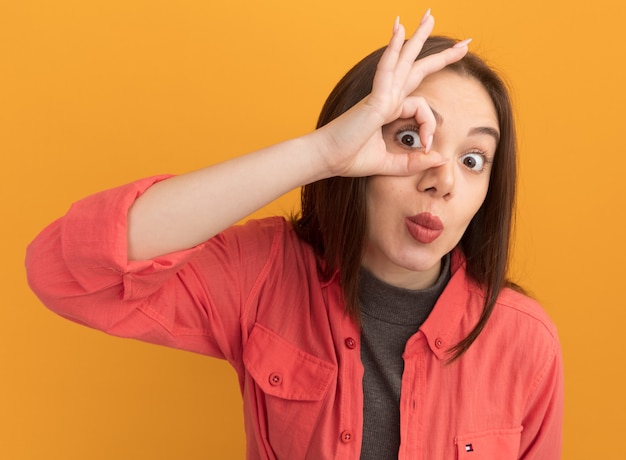 Photo gratuite jeune jolie femme impressionnée faisant un geste de regard isolé sur un mur orange