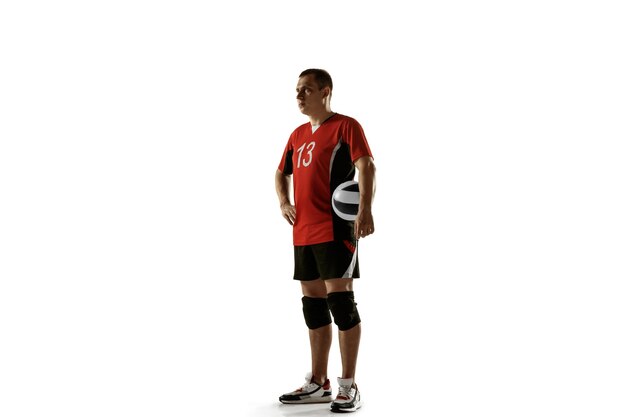 Jeune joueur de volley-ball caucasien pratiquant sur un mur blanc. Sportif masculin posant confiant avec le ballon, préparé pour la victoire. Sport, mode de vie sain, activité, concept de mouvement. Espace de copie.