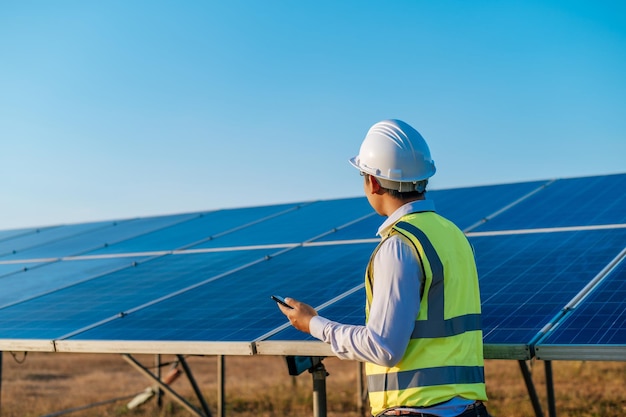 Jeune technicien asiatique homme debout et parlant sur smartphone entre de longues rangées de panneaux solaires photovoltaïques copie espace