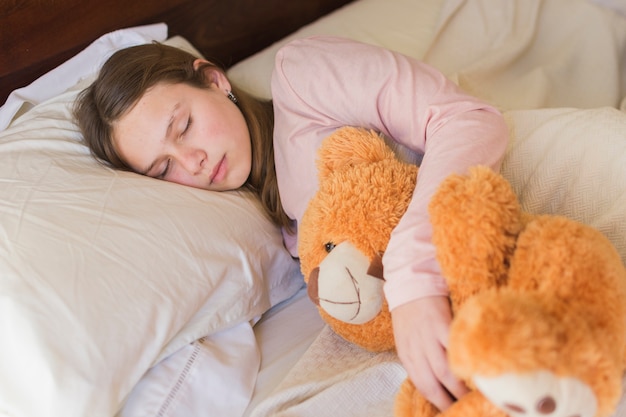 Photo gratuite jolie fille dormant avec un ours en peluche sur le lit