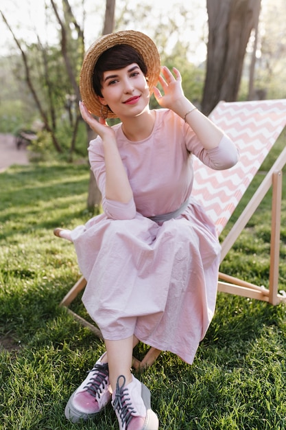 Photo gratuite jolie fille souriante en tenue à la mode bénéficiant d'un week-end et d'une vue magnifique sur la nature, assise sur une chaise de jardin