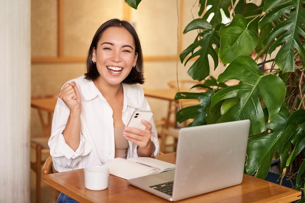 Photo gratuite joyeuse jeune femme asiatique gagnante en célébrant la victoire ou la réussite recevoir de bonnes nouvelles sur son téléphone portable