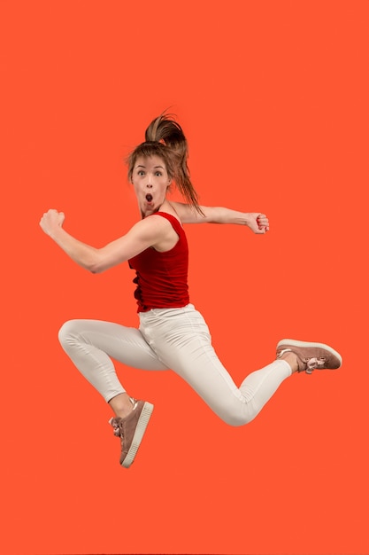 Photo gratuite liberté de mouvement. tir en l'air d'une jeune femme assez heureuse sautant et faisant des gestes sur fond de studio orange.