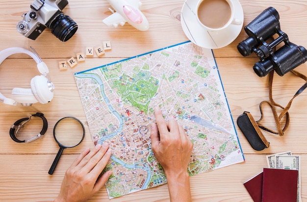 Photo gratuite la main de la personne pointant vers l'emplacement sur la carte avec une tasse de thé et des accessoires de voyageur sur une surface en bois