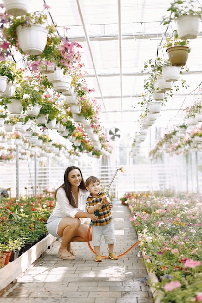 Photo gratuit maman et son fils avec un pulvérisateur d'eau dans la serre. petit garçon enfant arrosant des fleurs dans une serre