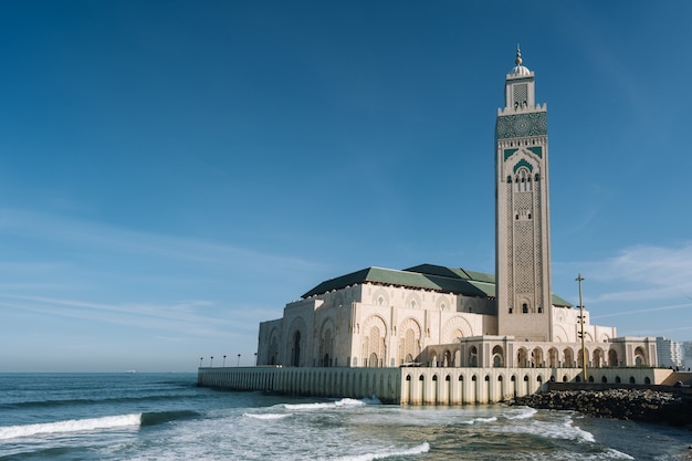 Photo gratuit mosquée hassan ii entourée d'eau et de bâtiments sous un ciel bleu et la lumière du soleil