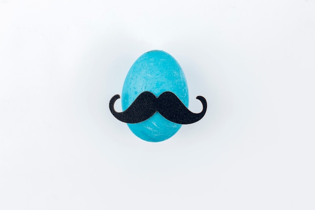 Photo gratuite oeuf de pâques bleu avec moustache en papier sur la table