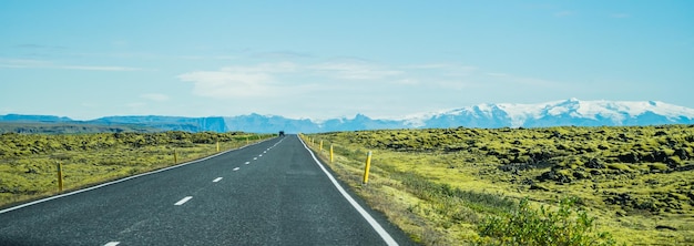 Photo gratuite panoramique d'une longue route goudronnée entourée de champs herbeux en islande