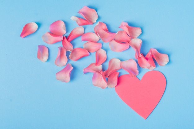 Pétales de roses avec coeur rose sur table