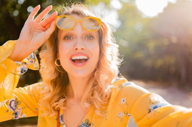 Photo gratuite portrait de la belle blonde élégante femme souriante en chemisier jaune portant des lunettes de soleil faisant selfie photo