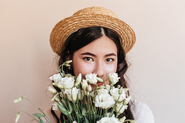 Photo gratuit portrait de femme coréenne tenant des fleurs et regardant la caméra. photo de studio de femme asiatique au chapeau de paille avec eustomas blancs.