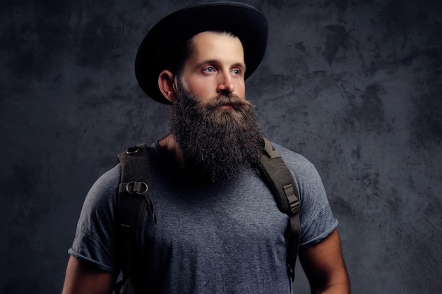 Photo gratuite portrait en gros plan d'un beau voyageur barbu en chapeau avec sac à dos. isolé sur un fond sombre.