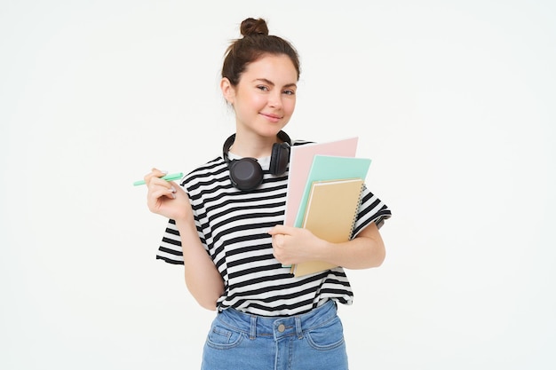 Photo gratuite portrait d'une jeune étudiante avec des cahiers et des écouteurs au cou posant pour l'université