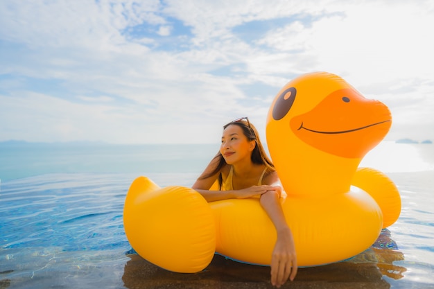 Photo gratuite portrait de jeune femme asiatique sur canard jaune gonflable flotteur autour de la piscine extérieure de l'hôtel