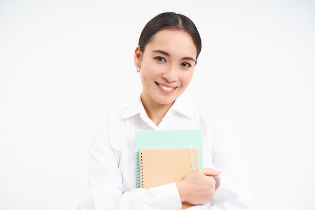 Photo gratuit portrait d'une jeune femme asiatique tuteur indépendant tient des cahiers et des travaux d'études se dresse sur ba blanc