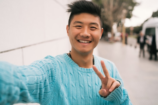 Photo gratuite portrait de jeune homme asiatique à la recherche de confiance et de prendre un selfie tout en se tenant à l'extérieur dans la rue.