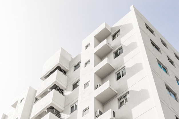 Photo gratuit prise de vue en contre-plongée d'une façade d'un immeuble moderne blanc sous un ciel bleu clair