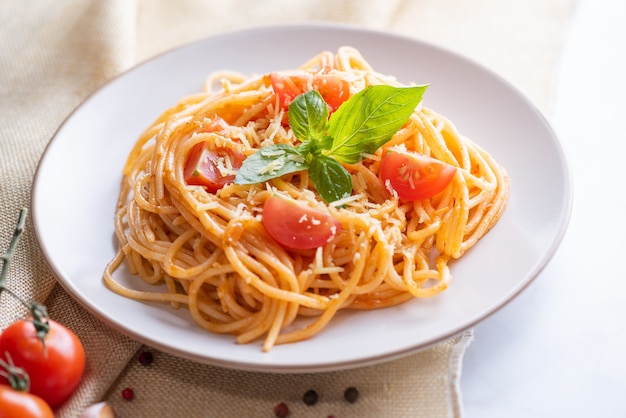 Photo gratuite savoureuses pâtes spaghetti italiennes classiques appétissantes avec sauce tomate, fromage parmesan et basilic sur assiette et ingrédients pour la cuisson des pâtes sur une table en marbre blanc.