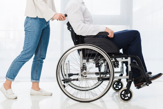 Section basse d'une femme poussant l'homme assis sur un fauteuil roulant