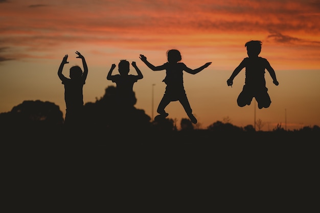 Photo gratuite silhouette d'enfants posant sur la colline entourée de verdure pendant un coucher de soleil doré