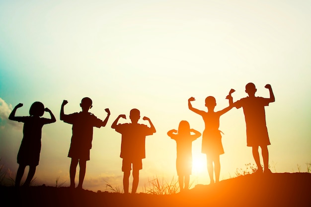 Photo gratuite les silhouettes des enfants montrant les muscles au coucher du soleil