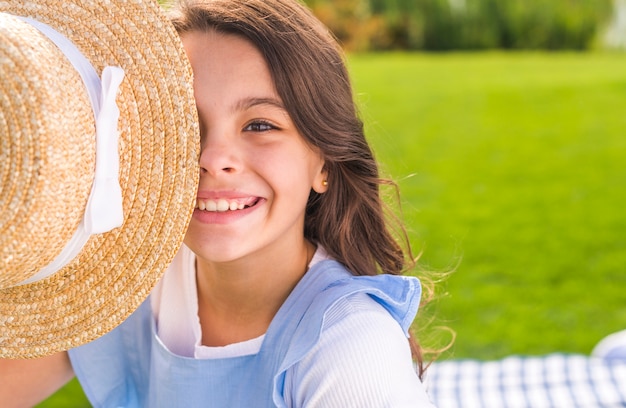 Photo gratuite smiley petite fille couvrant son oeil avec un chapeau de paille