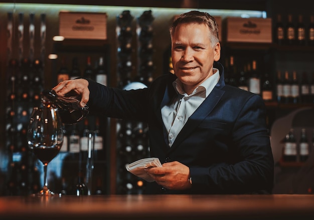 Photo gratuite un sommelier de vin élégant et soigné verse du vin rouge au verre pour le goûter.