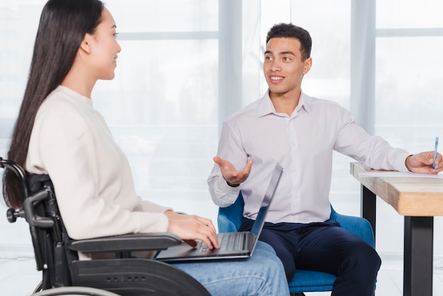 Souriant jeune homme d&#39;affaires et femme handicapée ayant des discussions au bureau