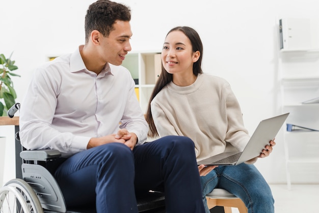 Photo gratuite souriante jeune femme montrant quelque chose à un homme d'affaires assis sur un fauteuil roulant