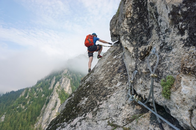 Photo gratuite superbe photo d'un jeune homme escalade une falaise par une journée froide et brumeuse