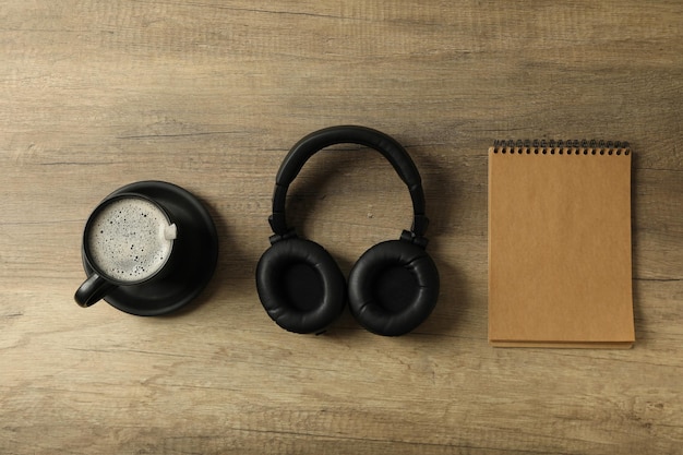 Photo gratuite une tasse de café avec des écouteurs et un bloc-notes sur un fond en bois