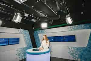 Photo gratuite télévision présente au studio se préparant pour une nouvelle diffusion. jeune fille souriante en chemise blanche assise à table.