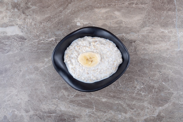 Photo gratuite tranches de banane mûre sur un bol de porridge, sur la surface en marbre