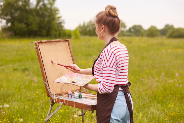 Photo gratuit vue arrière de la jeune femme artiste debout devant un carnet de croquis avec pinceau et palette de couleurs