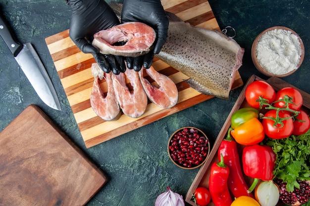 Vue de dessus chef tenant des tranches de poisson cru de légumes sur une planche de service en bois sur une table de cuisine