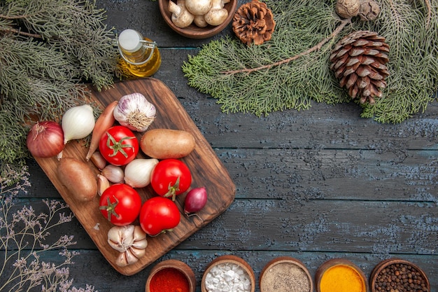 Vue de dessus des légumes et des branches de la planche à découper et des légumes dessus entre des épices colorées et un bol d'huile de champignons blancs et de branches d'épinette