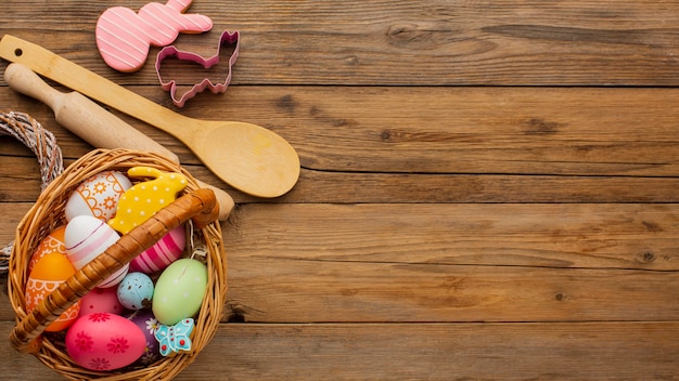 Vue de dessus des oeufs de Pâques colorés dans le panier avec des ustensiles de cuisine et de l'espace de copie