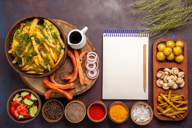 Photo gratuite vue de dessus des pommes de terre frites avec du pain d'assaisonnement et différents légumes sur le bureau sombre