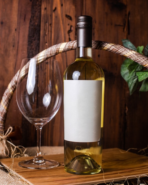 Photo gratuite une vue de face une bouteille de vin blanc avec du verre vide sur le bureau en bois