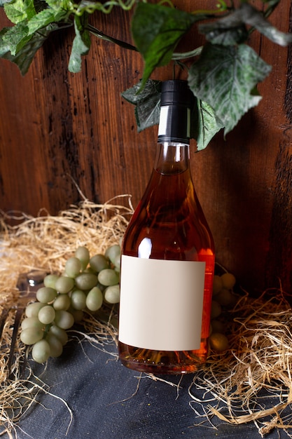 Photo gratuite une vue de face bouteille de whisky avec des raisins verts et des feuilles vertes isolatedo n le fond brun boire de l'alcool de cave