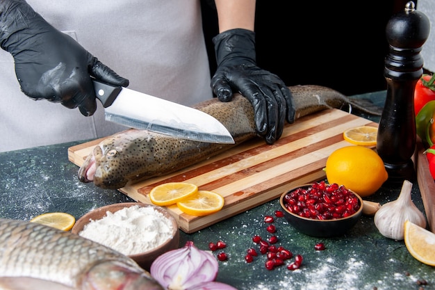 Vue de face chef hacher du poisson cru sur planche de bois moulin à poivre bol de farine graines de grenade dans un bol sur la table de la cuisine