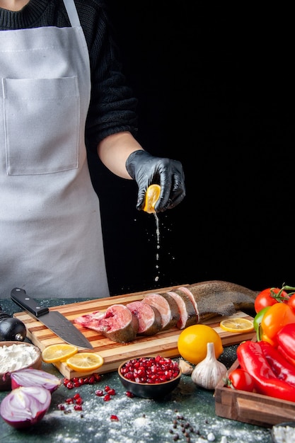 Vue de face chef pressant du citron sur des tranches de poisson cru couteau sur une planche à découper sur une table de cuisine