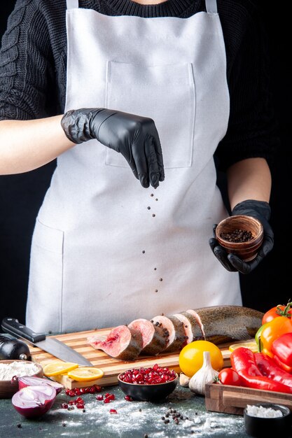 Vue de face le chef a saupoudré de poivre noir sur des tranches de poisson cru sur une planche à découper des légumes sur une planche de service en bois sur une table