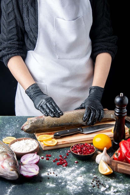 Vue de face chef en tablier blanc hacher du poisson cru sur planche de bois moulin à poivre bol de farine graines de grenade dans un bol sur la table de la cuisine