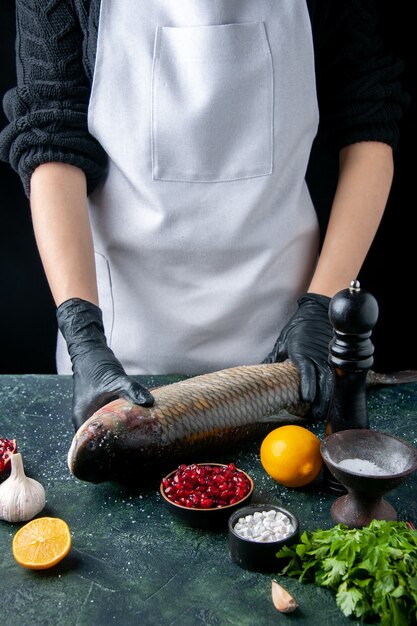 Vue de face chef en tablier mettant du poisson cru sur une planche à découper des graines de grenade moulin à poivre dans un bol sur la table