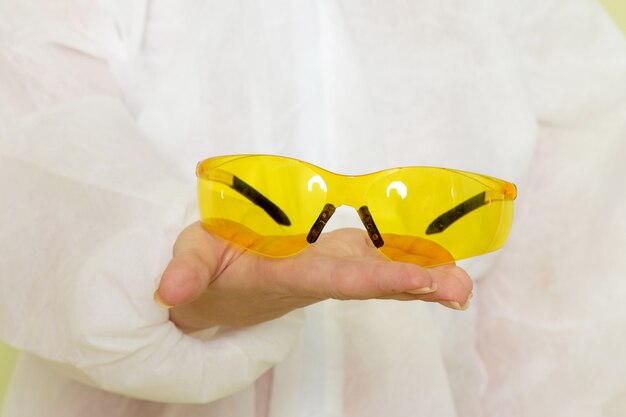 Vue de face jeune femme en costume spécial blanc et casque jaune tenant des lunettes de soleil spéciales jaunes sur l'emploi de l'espace vert