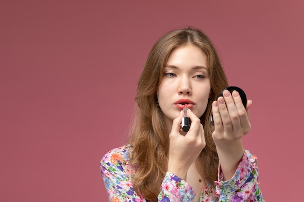 Photo gratuite vue de face jeune femme peignant ses lèvres avec du rouge à lèvres et à l'aide d'un mini miroir