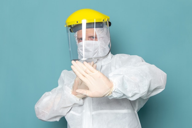 Photo gratuite une vue de face jeune homme en costume spécial blanc et casque spécial jaune en gardant la distance sur le mur bleu homme costume couleur équipement spécial danger