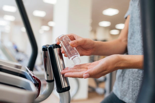 Photo gratuit vue latérale de la femme à l'aide de désinfectant pour les mains au gymnase pendant la pandémie