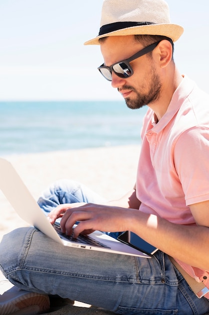 Vue latérale de l'homme avec un ordinateur portable à la plage